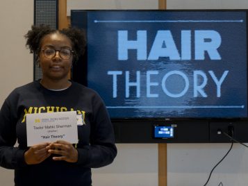 Taelor Sherman stands in front of a large monitor displaying her project, "Hair Theory."